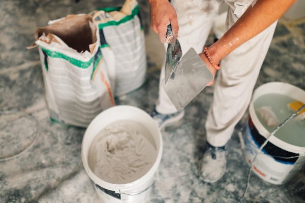 Close up of house painter's hands holding spatula and trowel while preparing for plastering and skim coating walls in a dusty and messy room in renovation process. A worker doing manual works in house