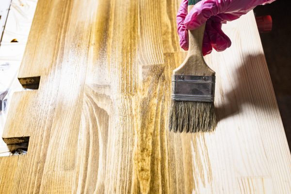 new wooden shelf is covered with wood stain by paint brush at home